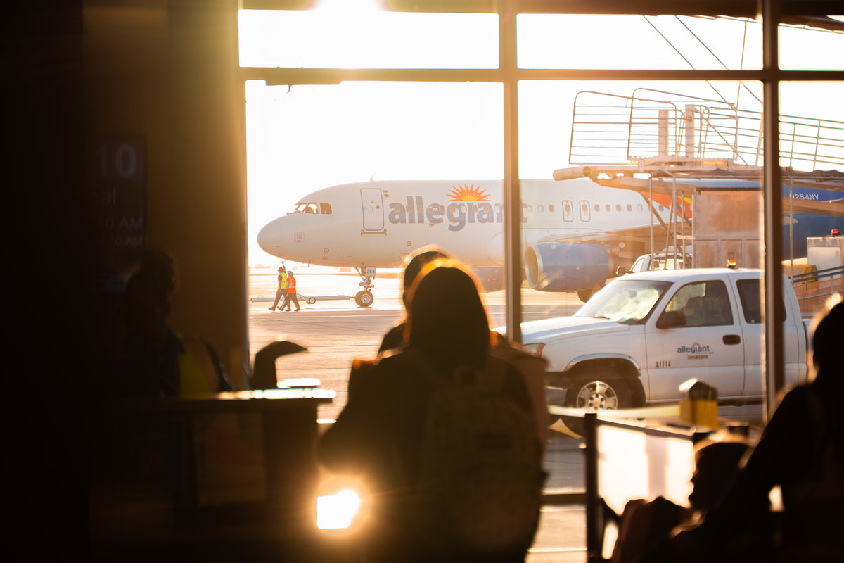 Allegiant airplane seen through an airport terminal window in warm sunlight