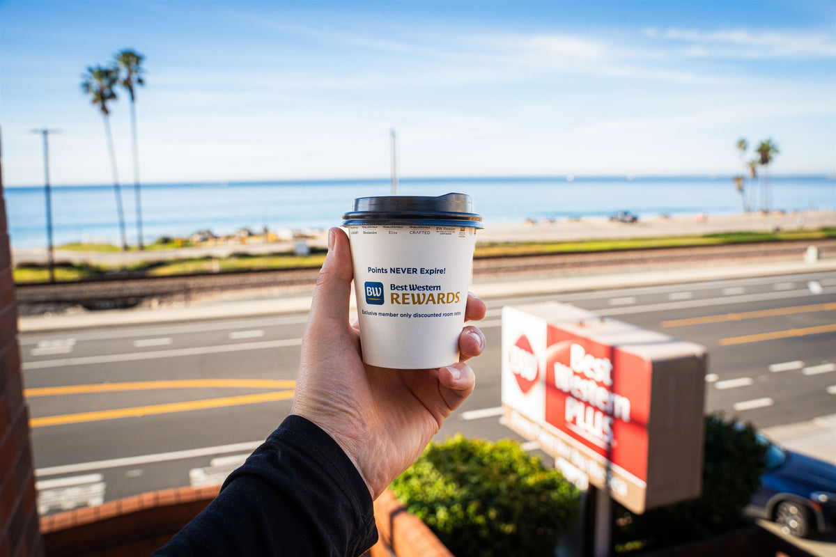 Best Western Rewards coffee cup held above a coastal view in Dana Point
