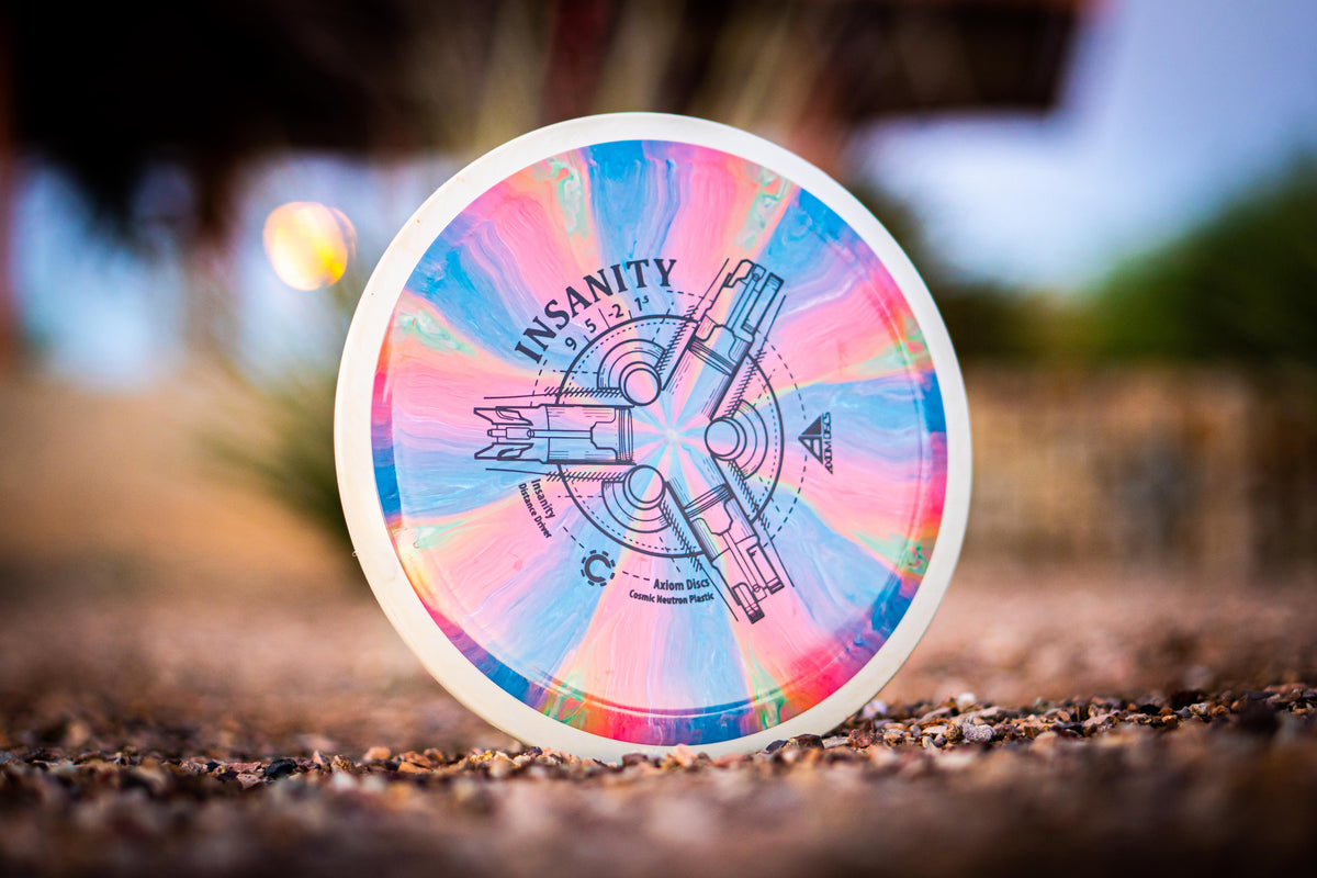 Pastel-colored Axiom Insanity disc photographed upright outdoors against a softly blurred background