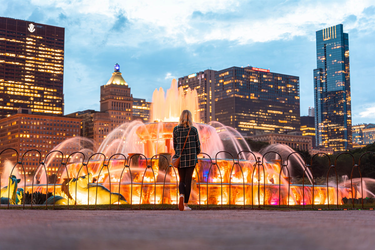 Traveler looking toward the illuminated Chicago fountain and skyline at dusk