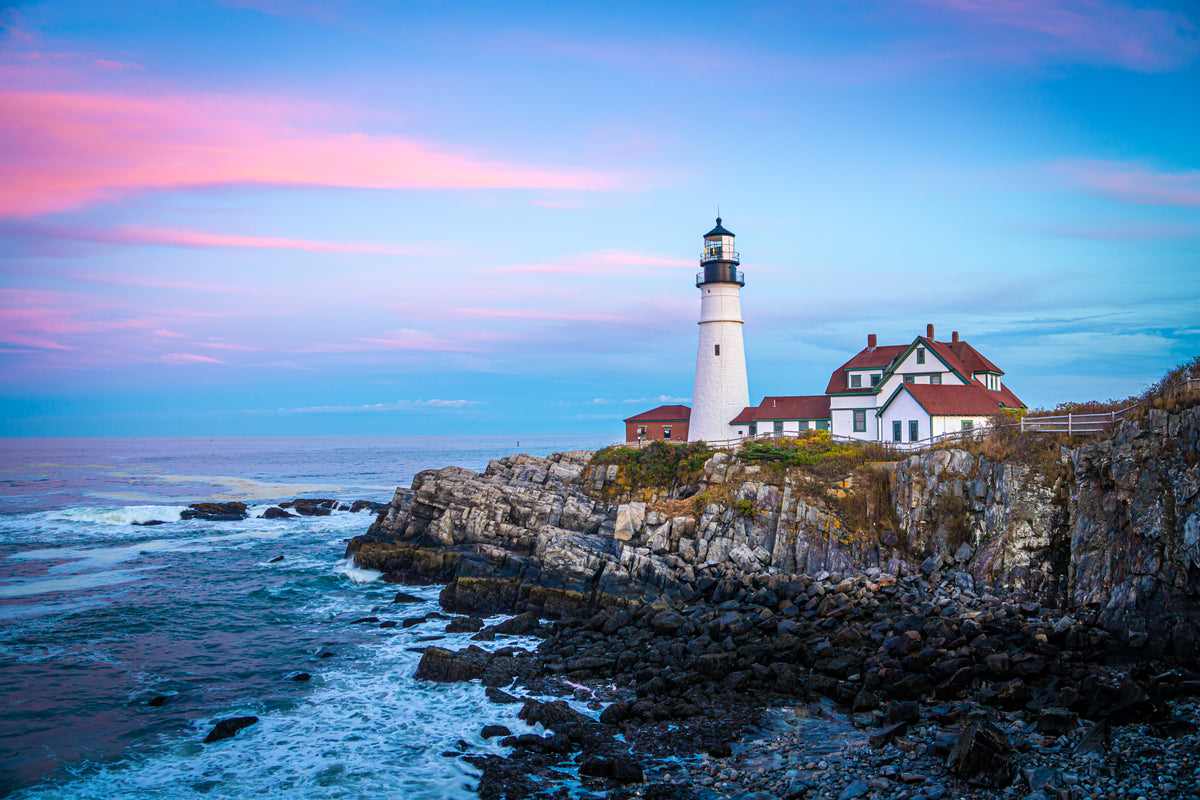 Lighthouse above Maine's rocky coastline beneath a pink and blue evening sky