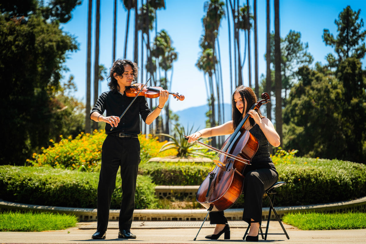 Violinist and cellist performing together in a palm-lined garden