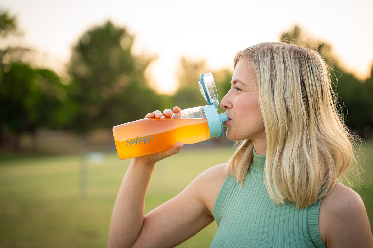 Woman drinking from an orange Swigg bottle in warm outdoor light