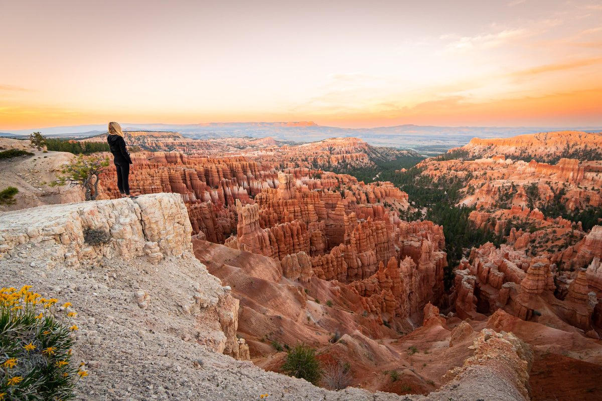 Traveler overlooking Bryce Canyon's orange rock formations beneath a warm sunset sky in Utah