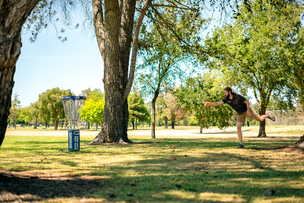James Conrad putting toward an MVP Disc Sports basket in a tree-lined park