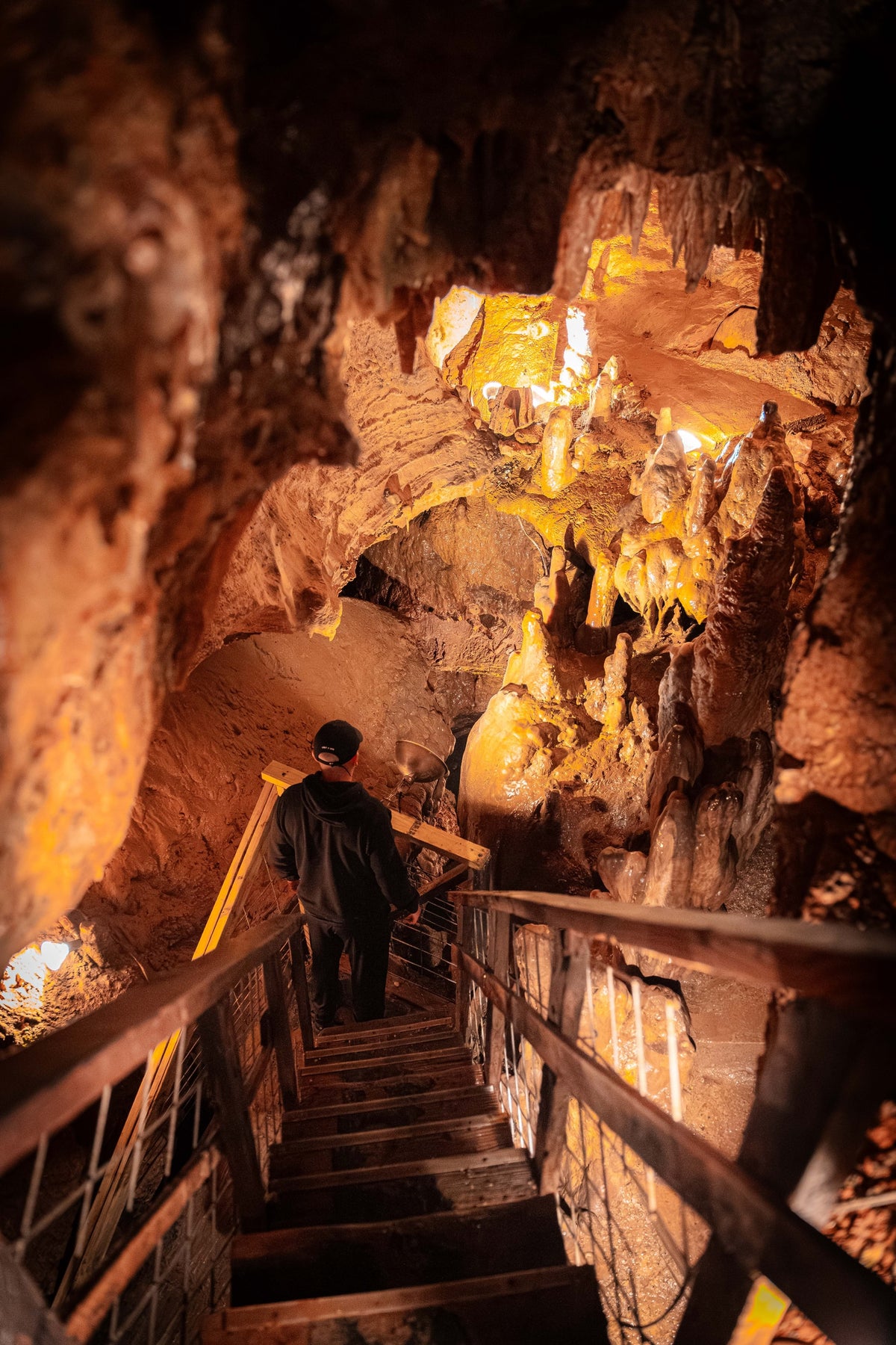 A visitor descending a railed staircase between warmly illuminated cave formations