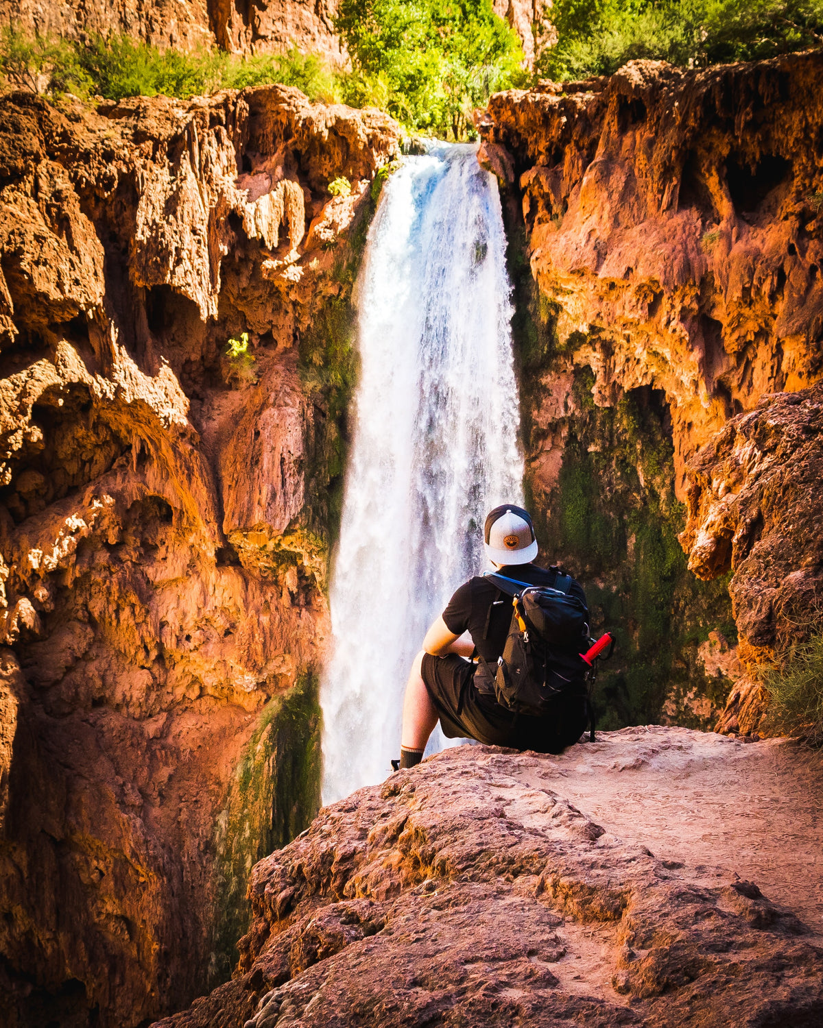Tyler Barks sitting with his backpack on a rock overlooking a waterfall in Havasupai