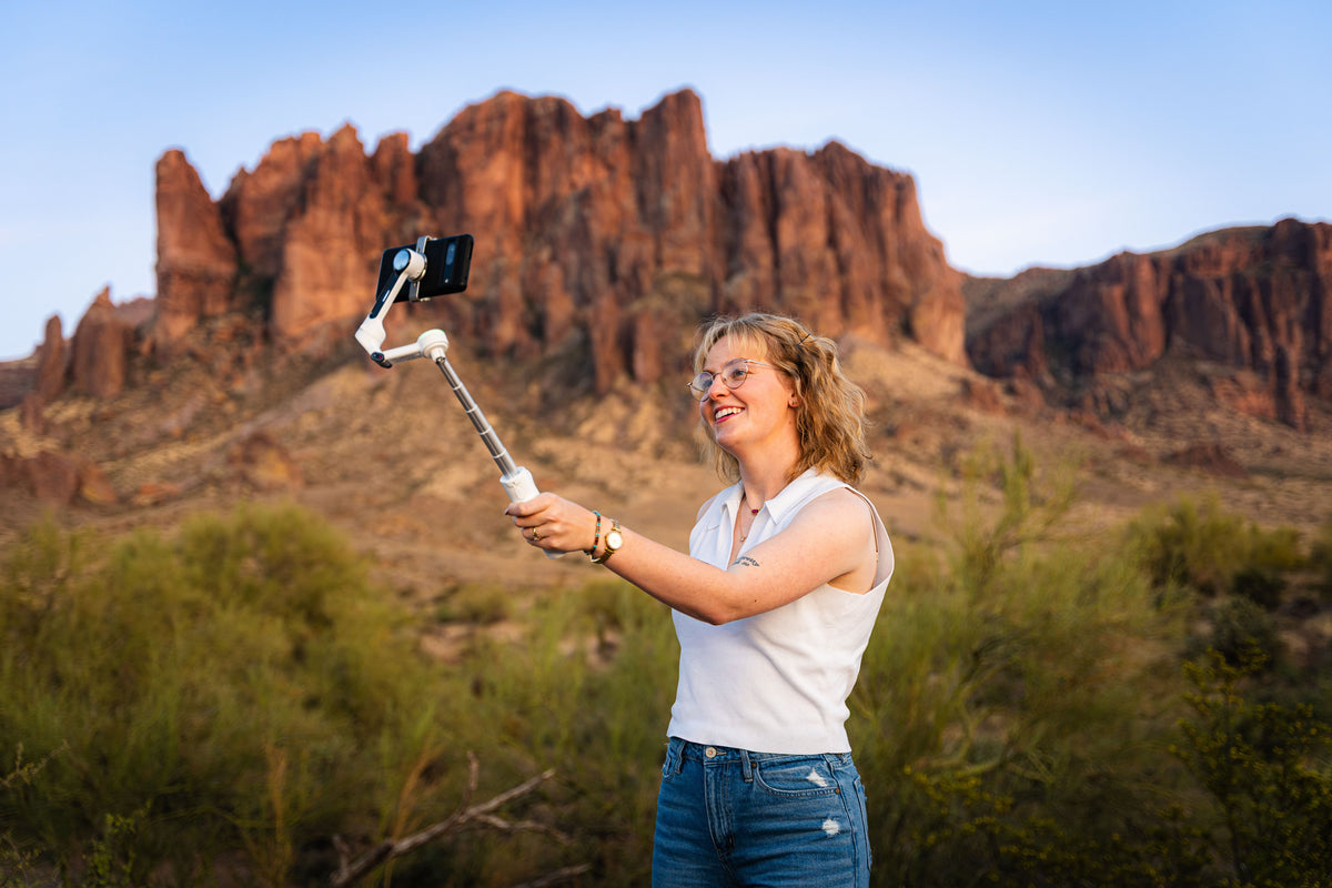 Woman using an Insta360 Flow 2 smartphone gimbal in front of red rock mountains in the desert