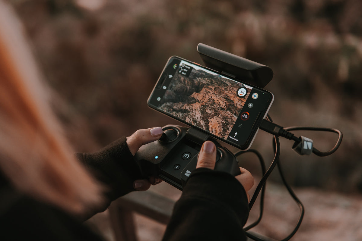 Hands operating a Skydio drone controller with a phone showing the view over a rocky landscape