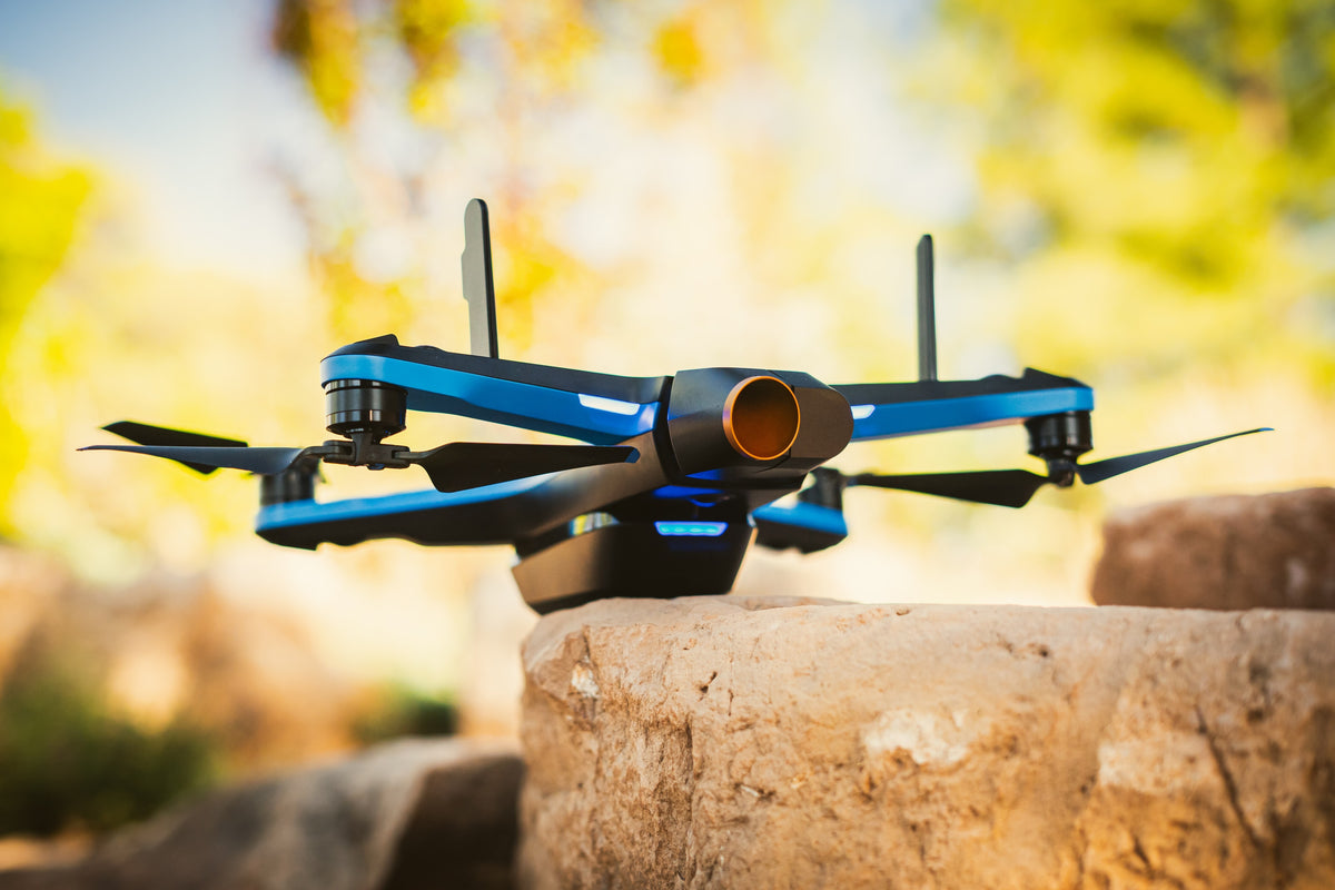 Blue and black Skydio drone photographed close up on a rock against a softly blurred golden background