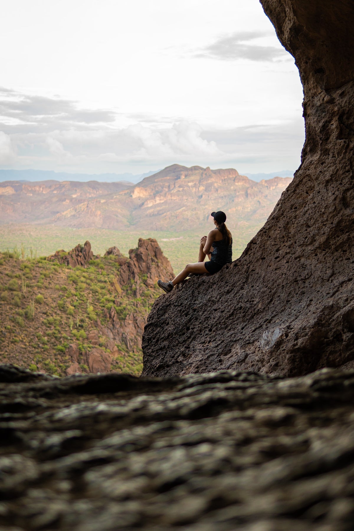 A seated visitor beside the textured Wave Cave wall looking toward desert mountains